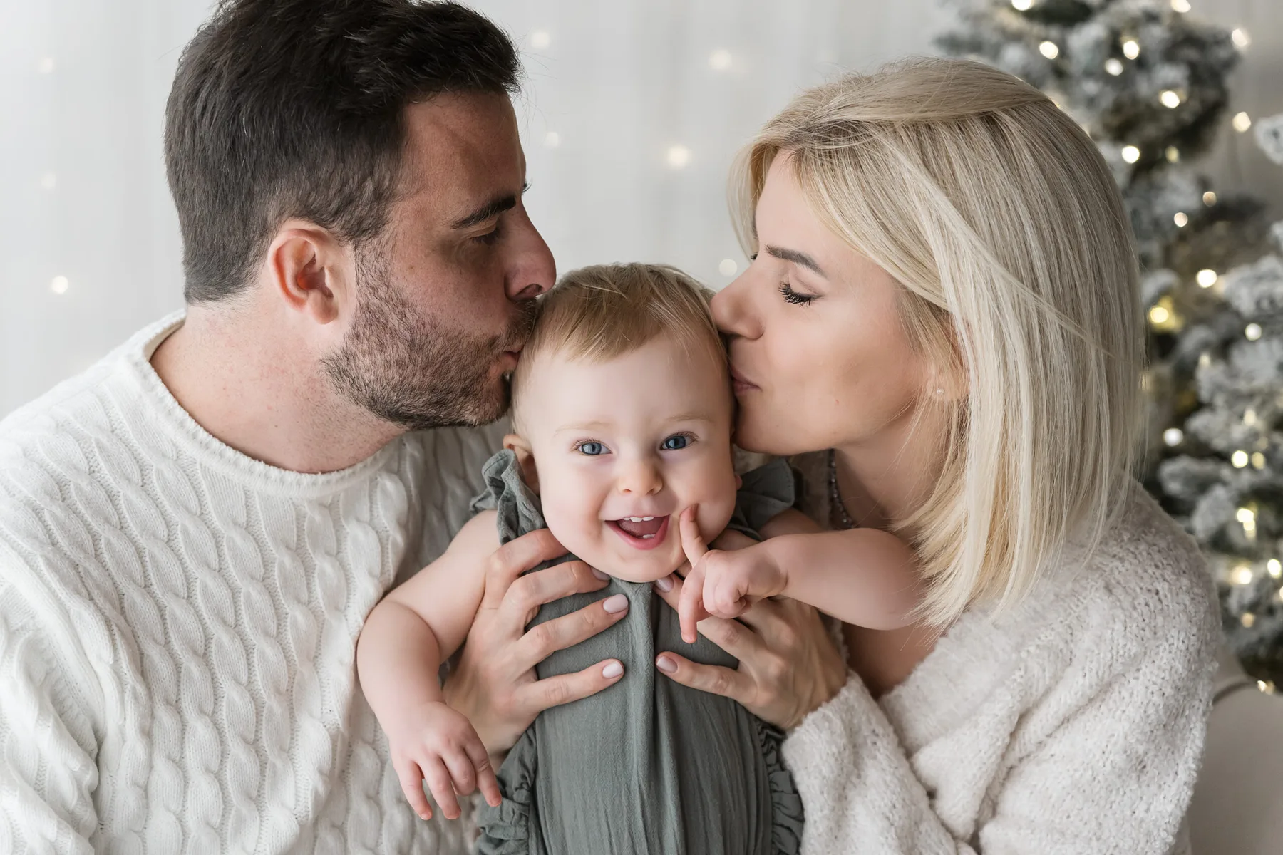 Mamma e papà baciano sulle guance il loro bambino nel set di Natale dell'Atelier di Livorno